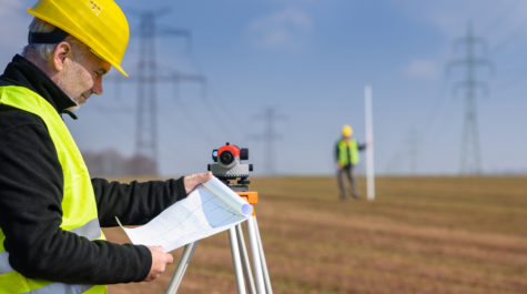 Land,Surveyors,On,Construction,Site,Reading,Plans,Wear,Reflective,Clothing
